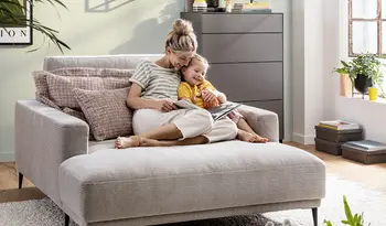 blonde Frau mit Kind schaut Möbelkatalog auf Sofa